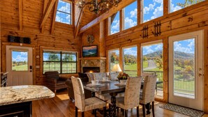 A wooden cabin interior with a dining area, fireplace, large windows, and a view of the outdoors. - Picture Perfect , Panoramic Mountain Views, $560 FREE tickets each paid day! (Sevierville)