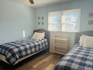 A bedroom with two beds, a window with blinds, and a wooden shelf.