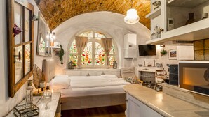 Una habitación acogedora con cama, ventana con vidrieras, zona de cocina y un techo original de ladrillo.
