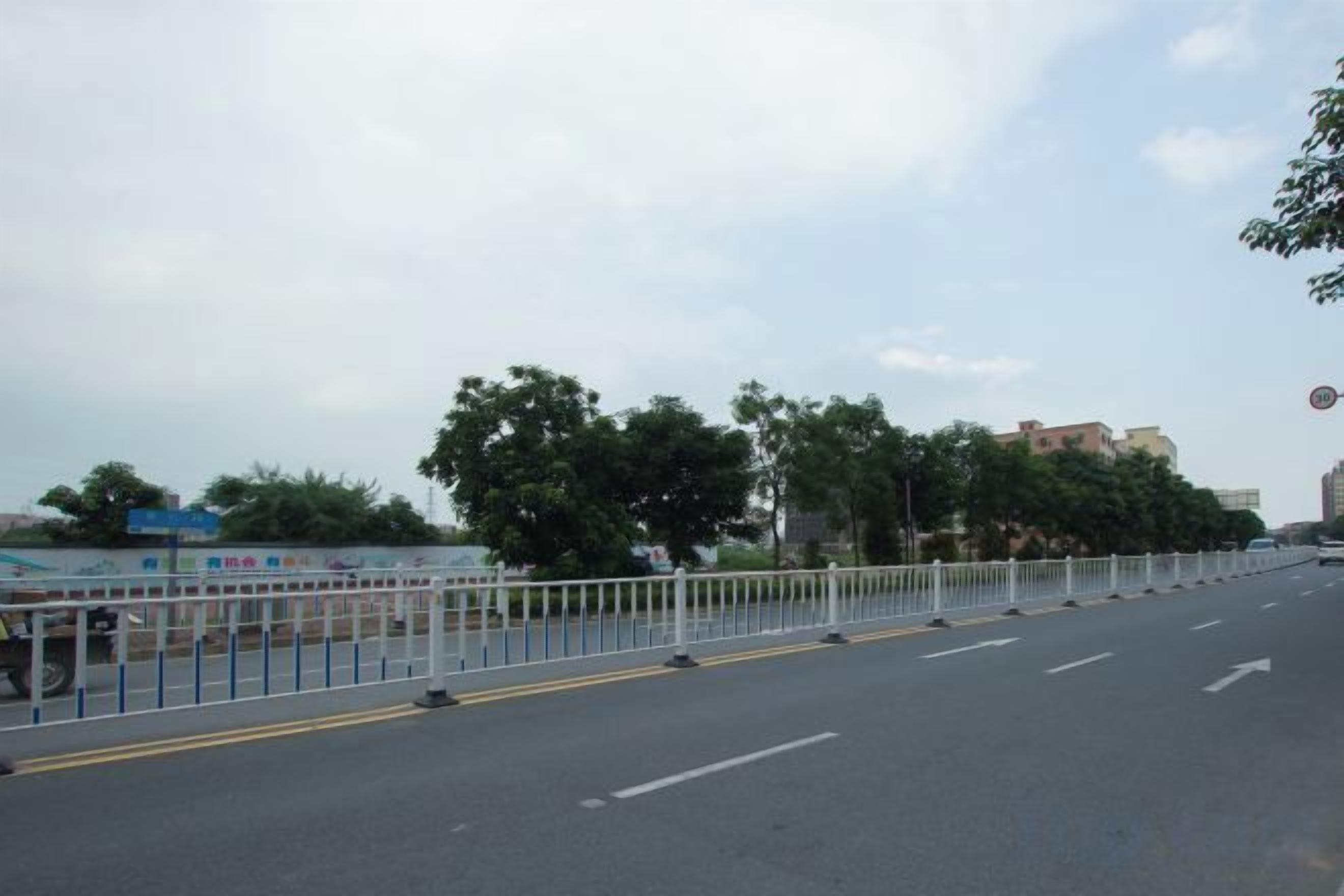 A road with a white fence, trees, and buildings in the background.