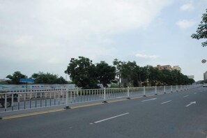 A road with a white fence, trees, and buildings in the background. - Qisheng Hotel (Dongguan)