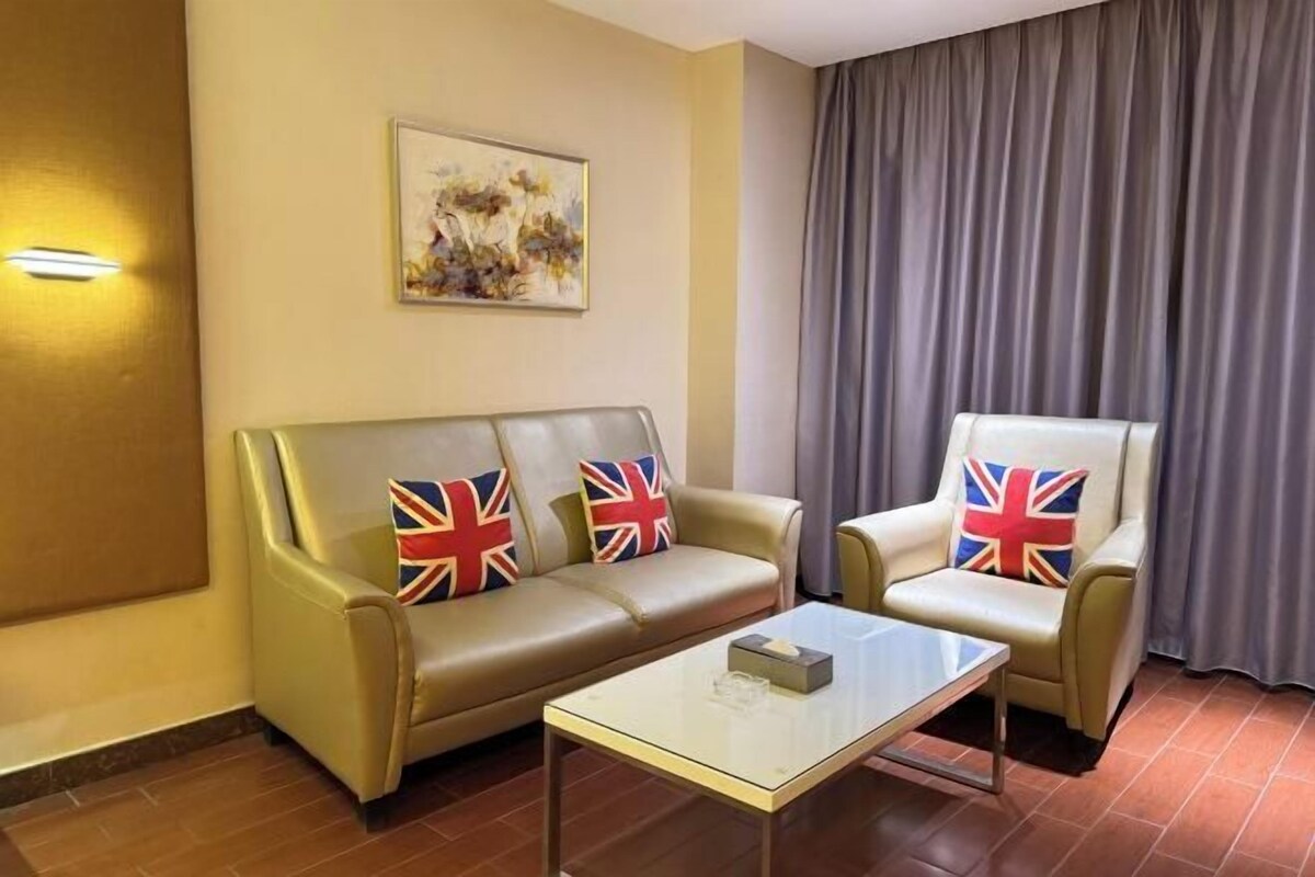 Et værelse med en sofa og en lænestol, begge med pude med britisk flag, et sofabord i glas samt et billede på væggen.