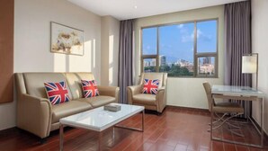A modern living room with a sofa set, a glass coffee table, a dining table with chairs, and a large window with a city view. - Qisheng Hotel (Dongguan)