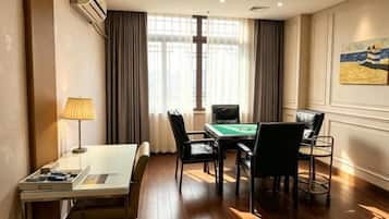 A hotel room with a pool table, a desk with a lamp, and a view of the outdoors through large windows.