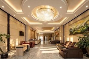 A spacious lobby with a chandelier, seating area, and a kitchen in the background. - Qisheng Hotel (Dongguan)