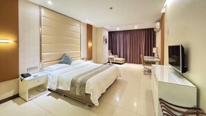 A modern hotel room with a large bed, bedside table, TV, and a small desk area. - Qisheng Hotel (Dongguan)