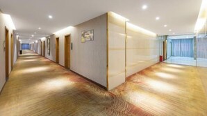 A long, well-lit hallway with wooden floors and doors on both sides, leading to a room with a large window and curtains. - Qisheng Hotel (Dongguan)