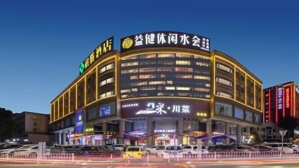 A multi-story hotel with a curved facade, illuminated signage, and a parking lot in front. - Qisheng Hotel (Dongguan)