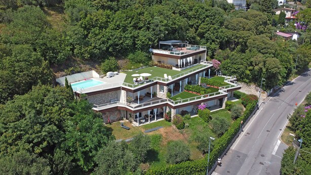 A multi-story house with a rooftop pool, surrounded by lush greenery.
