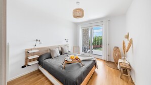 A modern bedroom with a large bed, bedside tables, a bedside lamp, a tray with breakfast items, a large window with a view of greenery, and a hanging light fixture.