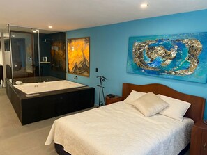 A bedroom with a large bed, a bathtub, and a glass-enclosed shower area.