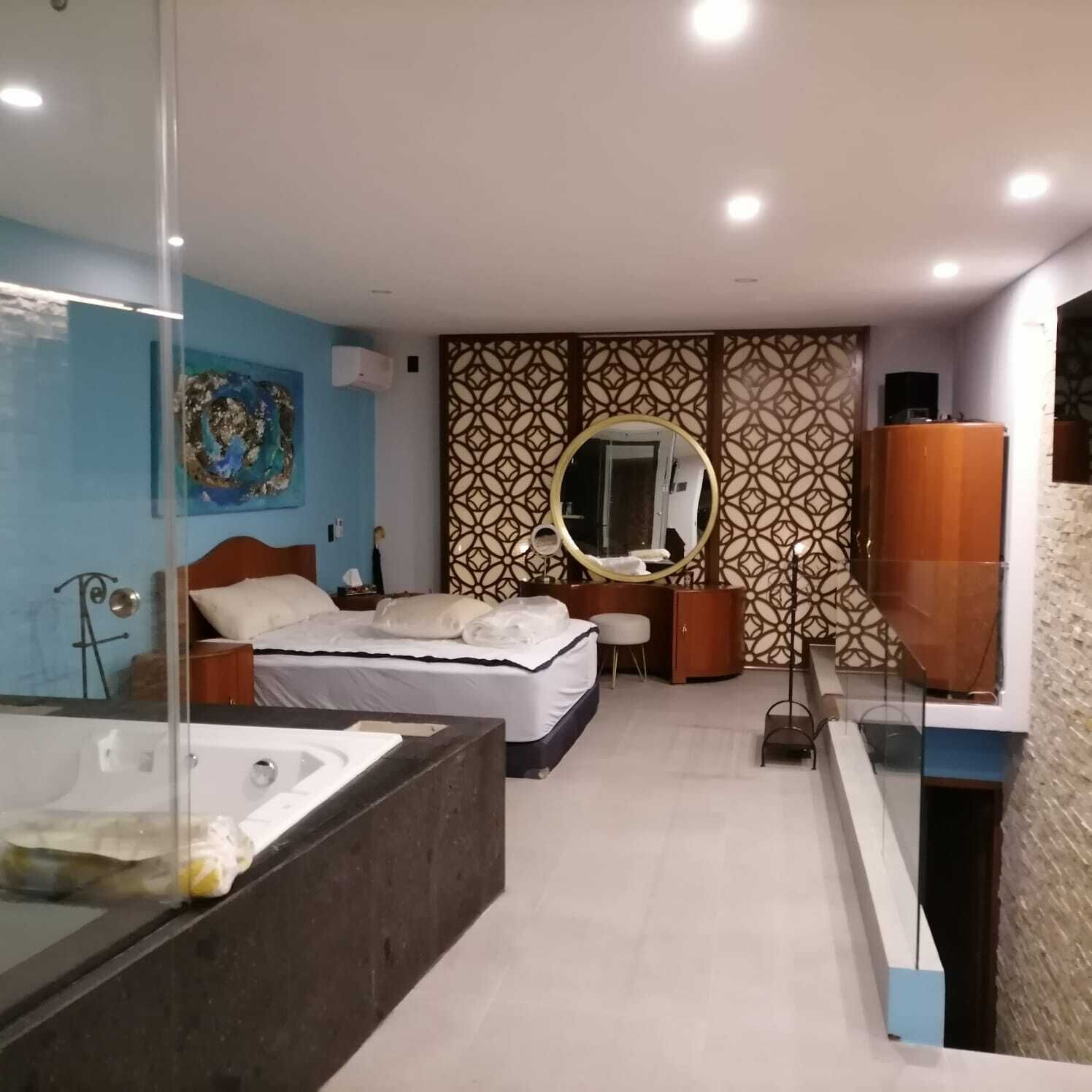 A modern hotel room with a large bed, a separate bathroom with a bathtub, and a large mirror.