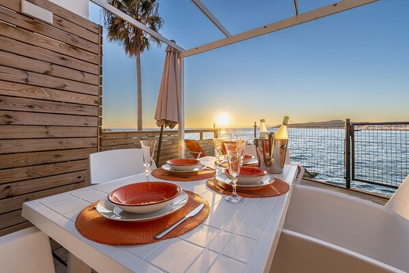 A dining table set for two with a view of the sea at sunset.