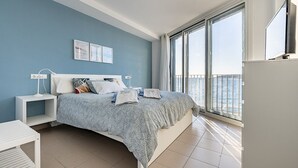 A modern bedroom with a large bed, a nightstand, a TV, and a view of the sea through large windows. - Casa LÁugusta II, House by the Sea in Altafulla (Altafulla)