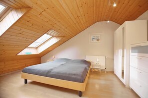 Een slaapkamer met een schuine kap, een bed, een radiator en een kledingkast.