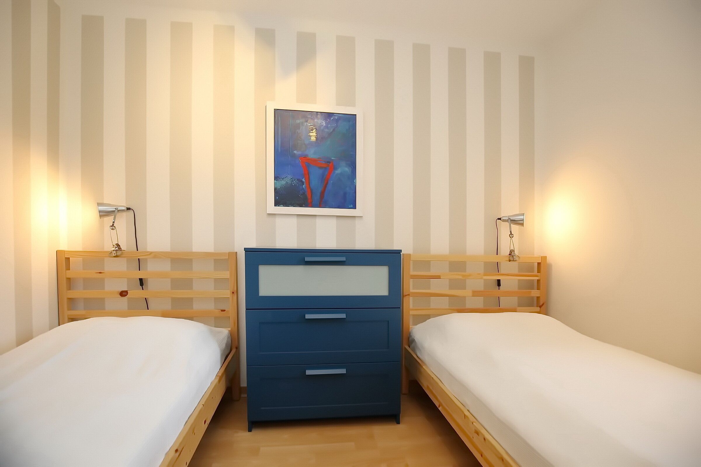 Un dormitorio con dos camas individuales, un aparador azul y un cuadro en la pared.