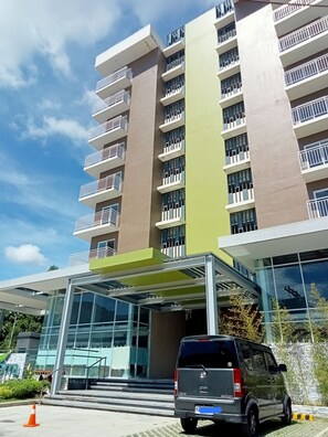 A multi-story hotel with a modern design, featuring a glass entrance and a parking area with a vehicle.