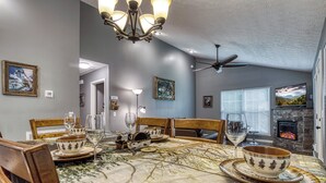 Comedor con mesa dispuesta para cuatro personas, candelabro, ventilador de techo y chimenea.