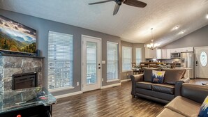 Ein geräumiges Wohnzimmer mit Kamin, Deckenventilator und einer Küche im Hintergrund.