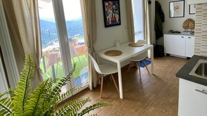 Un coin repas avec une table et des chaises, une cuisine équipée d’un évier et une vue sur un jardin grâce à de grandes fenêtres.