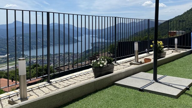 Un balcon avec un revêtement de gazon synthétique, une rambarde en métal et une vue sur un lac et des montagnes.