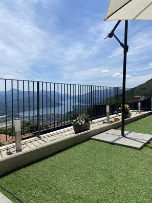 Un balcon avec un revêtement de gazon synthétique, une rambarde en métal et une vue sur un lac et des montagnes.