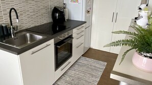 Une cuisine moderne avec des meubles blancs, un évier en acier inoxydable, une machine à café noire et un réfrigérateur décoré d’aimants.