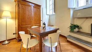 A dining area with a wooden table and white chairs, a wooden cabinet, a floor lamp, and a potted plant. - "Ricasoli Premium" open space (Firenze)