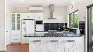 Une cuisine moderne avec des armoires blanches, un dosseret de carreaux noirs, une hotte de cuisinière en acier inoxydable, un four à micro-ondes encastré et une grande fenêtre donnant sur un paysage verdoyant.
