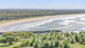 Un paysage côtier avec une plage de sable, une côte rocheuse et une végétation luxuriante au premier plan.