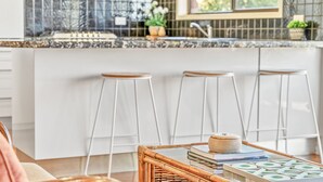 Une cuisine avec des meubles blancs, un plan de travail en marbre et trois tabourets blancs.