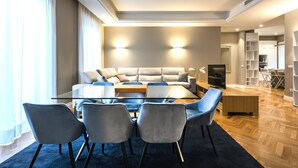 Un salon moderne avec une table basse en verre, des fauteuils à revêtement gris, un canapé gris et un téléviseur.
