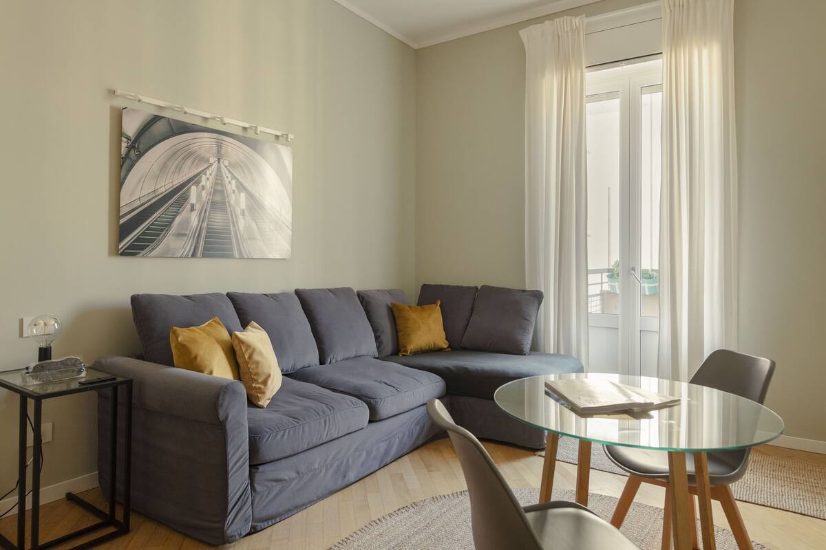 Una sala de estar moderna con un sofá seccional gris, una mesa de centro de vidrio y una mesita auxiliar.
