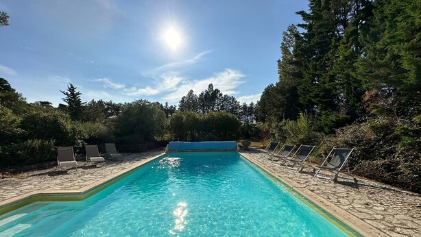 Une piscine d’un bleu éclatant, dotée de chaises longues et bordée d’une terrasse en pierre.