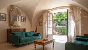Habitació amb un sofà verd, una taula de centre de fusta i un mirall gran. Hi ha una porta que condueix a una zona exterior amb vegetació.