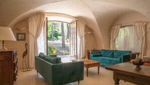 Habitació acollidora amb un sofà verd, una taula de fusta i vista a un jardí a través d'una finestra gran.