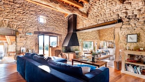 Un intérieur rustique en pierre, avec un grand canapé, des poutres en bois et une cheminée.