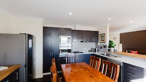 A modern kitchen with a built-in oven, microwave, and gas stove. There is a wooden dining table with chairs. - Jackson Hole 3 - 3/123 Gippsland Street (Jindabyne)