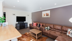 A modern living room with a brown leather sofa, a wooden coffee table, a flat-screen TV on a black stand, and a cowhide rug. - Jackson Hole 3 - 3/123 Gippsland Street (Jindabyne)