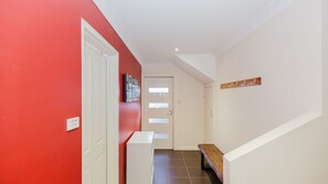 Un pasillo con pared roja, puerta blanca, un banco y un perchero.