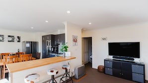 A modern kitchen with dark cabinets, a wooden dining table, and a flat-screen TV. - Jackson Hole 3 - 3/123 Gippsland Street (Jindabyne)