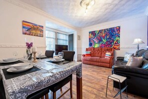 A dining area with a table set for four, a sofa, and a colorful abstract painting on the wall. - The Miracle Spacious 2 Bedroom 3 Beds Central Hull (Kingston upon Hull)