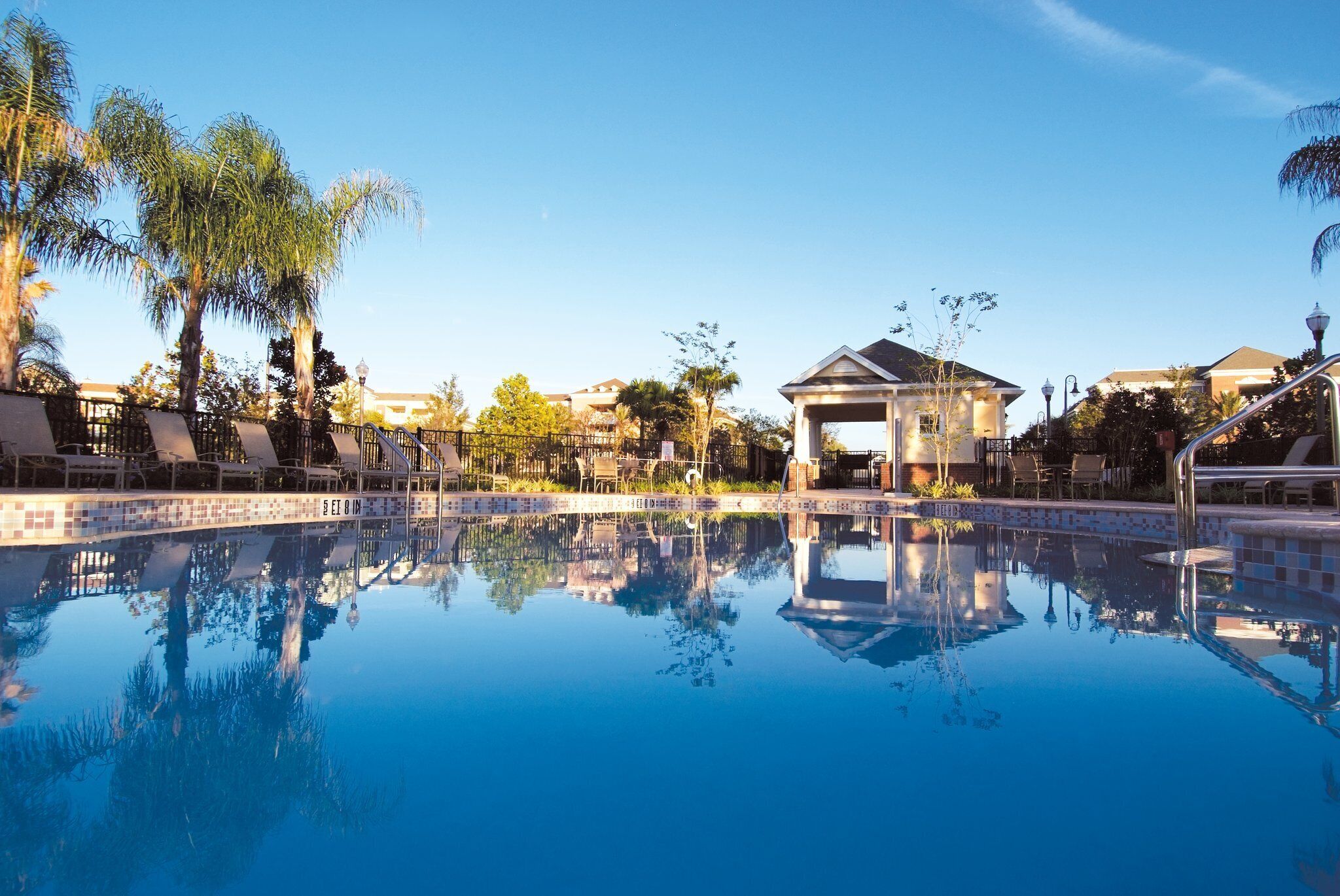 A clear pool with reflections, lounge chairs, and a gazebo.