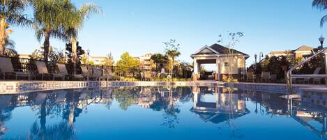 A clear pool with reflections, lounge chairs, and a gazebo.