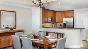 A modern kitchen with wooden cabinets, stainless steel appliances, and a dining area with a wooden table and chairs. - Worldmark Reunion (Kissimmee)