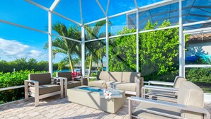 A sunlit patio with outdoor furniture, a fire feature, and a glass enclosure. - Intervillas Florida - Villa Brightwater  (Cape Coral)