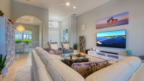 A modern living room with a large flat-screen TV, comfortable seating, and a view of the ocean. - Intervillas Florida - Villa Brightwater  (Cape Coral)