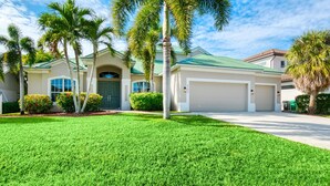 A two-story house with a green roof, a garage, and a well-maintained lawn with palm trees. - Intervillas Florida - Villa Brightwater  (Cape Coral)