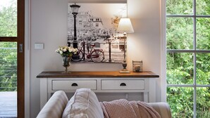 Una habitación con una cama, una mesita de noche con lámpara, un jarrón con flores y un cuadro en la pared de una bicicleta y un farol.