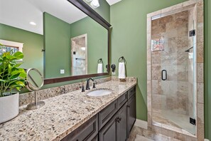 A bathroom with a granite countertop, a sink, a mirror, a potted plant, and a shower area with a glass door. - Wildside Retreat | Lake James | Pool & Resort Community Access | 3 BR | Pet-Friendly (Nebo)